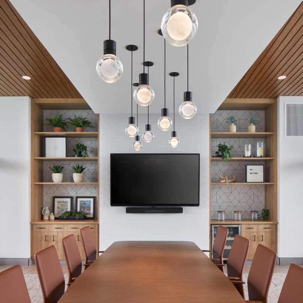 office conference room with natural wood tones, handing pendant lights, built-in shelves, and window walls on either side of room